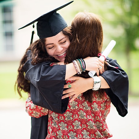 Young graduate smiles and hugs mother.