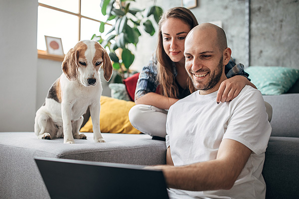 student with their partner and dog sitting on a couch and looking at a laptop computer