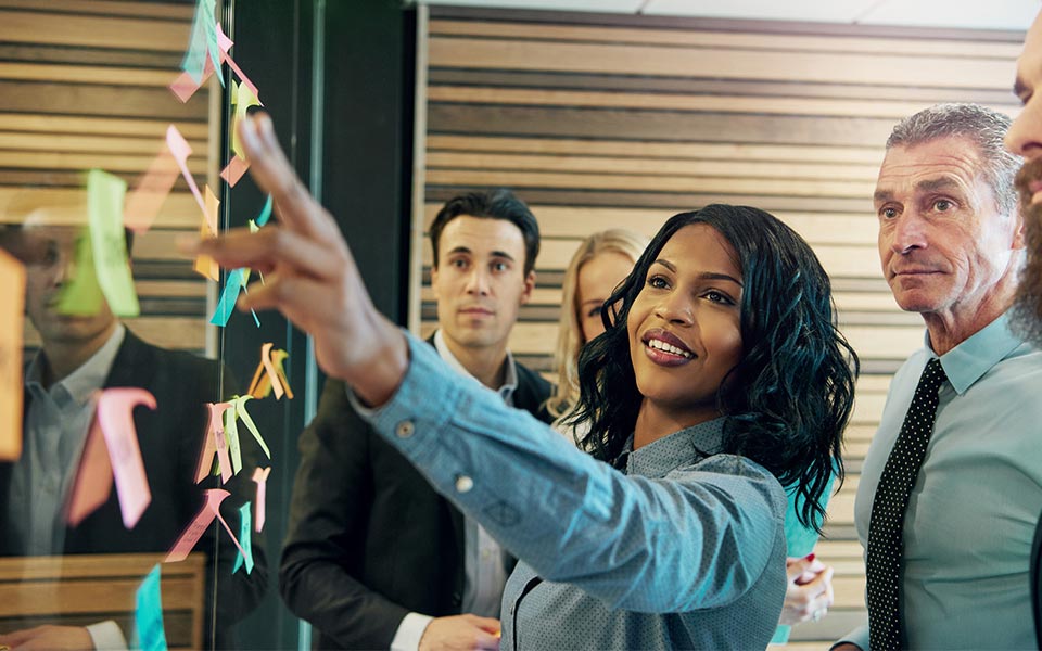 Team watches as leader points to board covered in colorful sticky notes