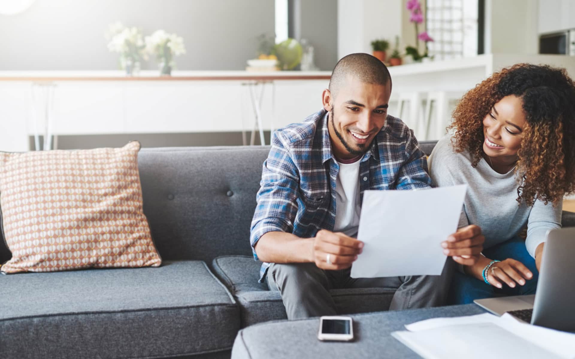 An African American couple sit on a couch happily reviewing paperwork.