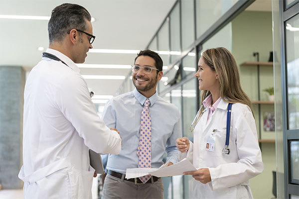 three healthcare professionals smiling and talking and shaking hands