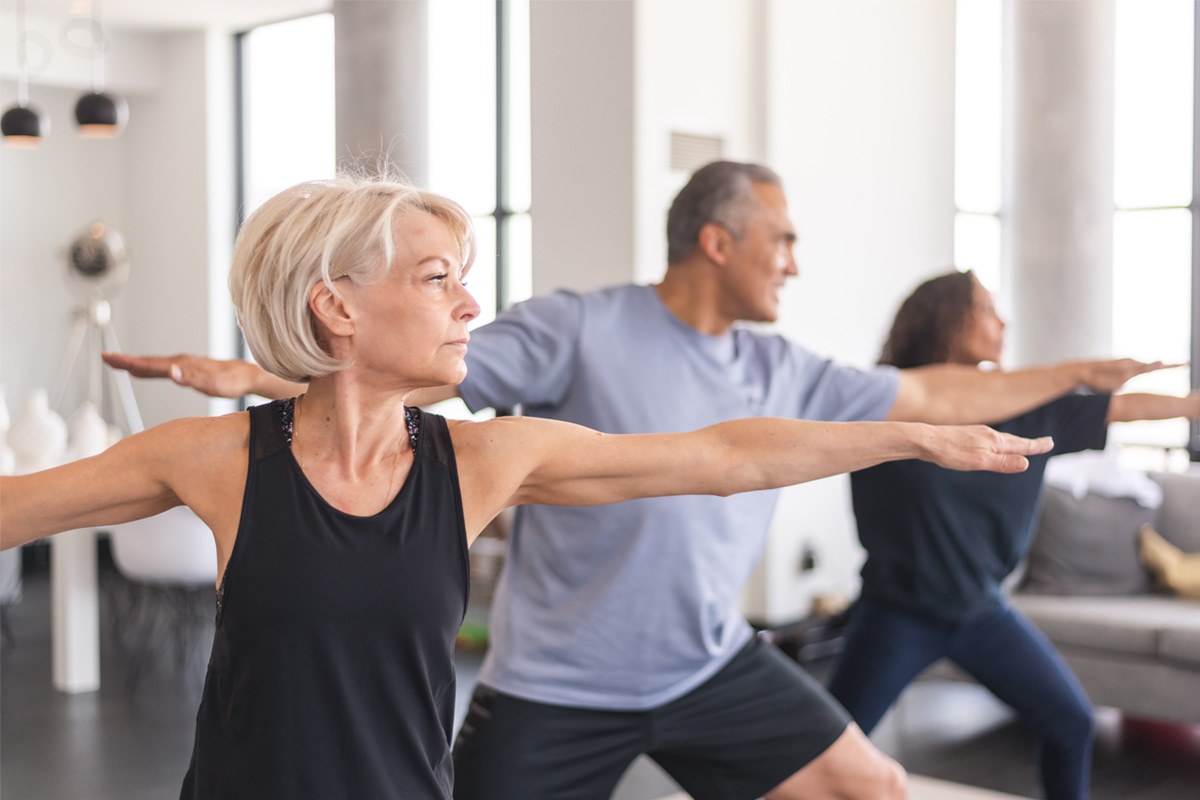 An older woman holds a warrior two pose in a group yoga class.