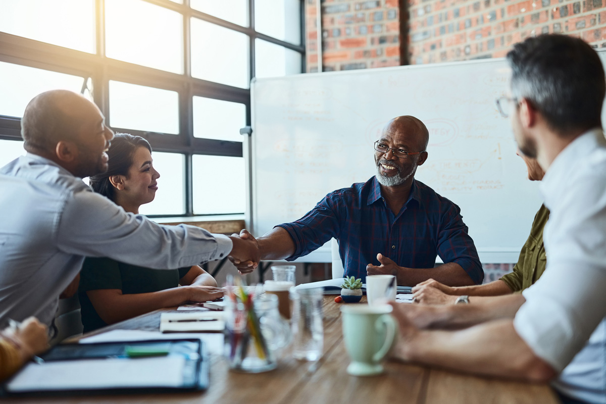 smiling manager sitting at table and meeting with team of employees and shaking hands with one