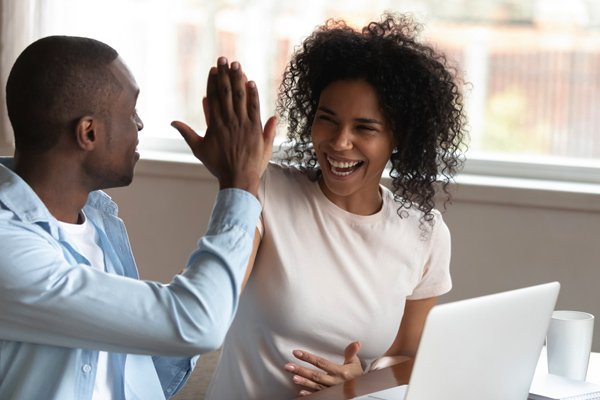 A couple high fives at a desk with a laptop.