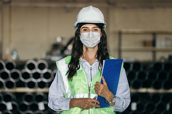 Safety Officer wearing helmet, facemask, and neon vest holding clipboard