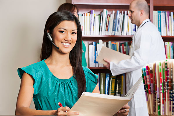 Cheerful medical billing and coding specialist looks up from an open folder.