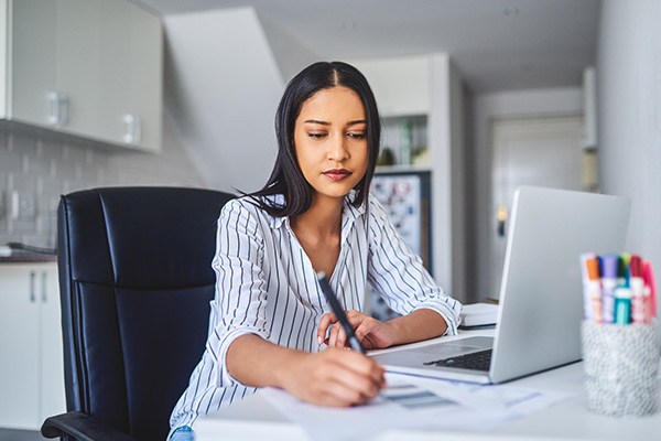 A young woman writes as she sits at her laptop.