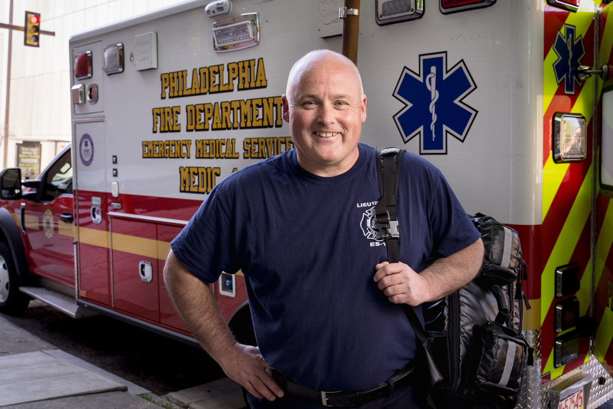 EMS professional holding a bag and standing in front of an ambulance from the Philadelphia Fire Department