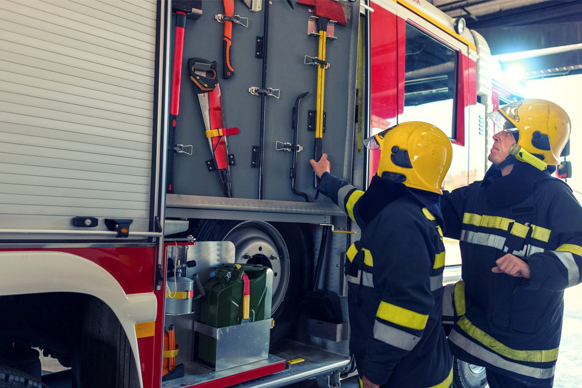 A firefighter reaches for an axe among a variety of equipment stowed in a fire truck