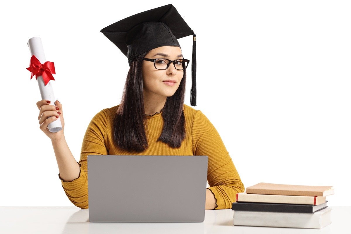 Young woman wearing a graduation cap holds a diploma tied with a bow