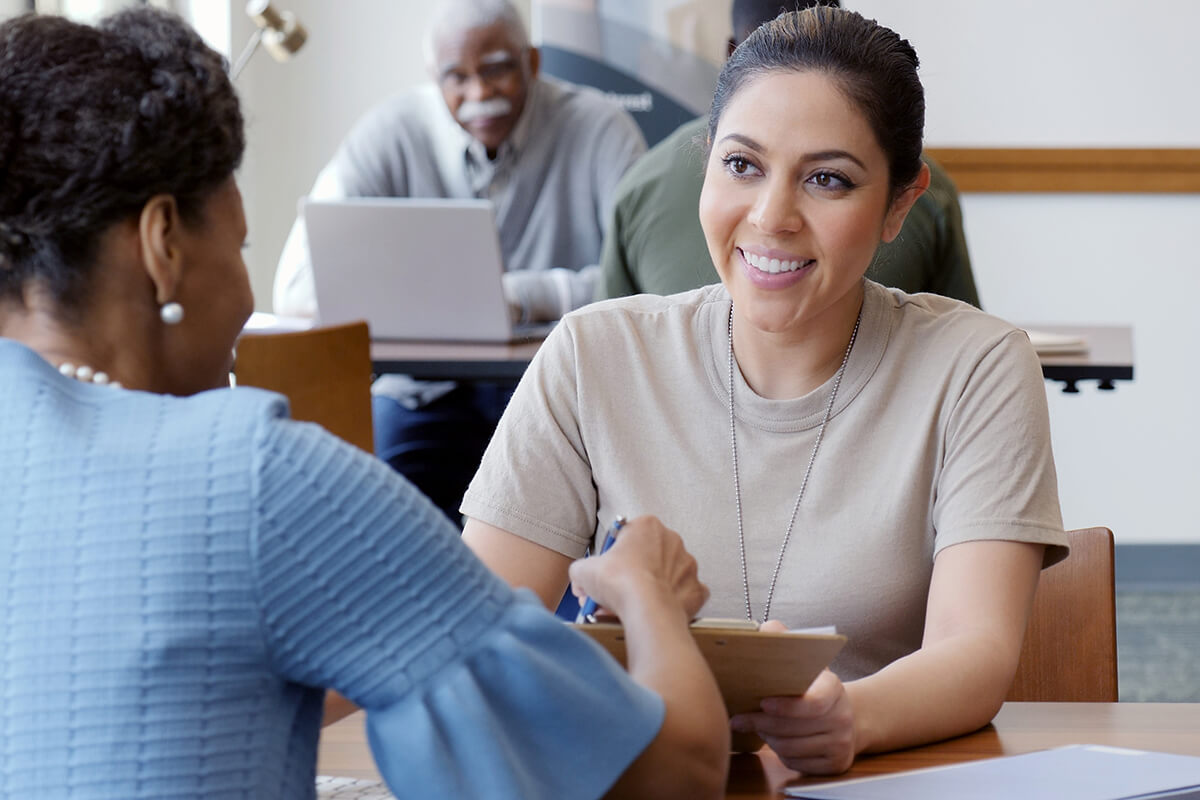 An off duty military woman meets with another woman as they review paperwork.