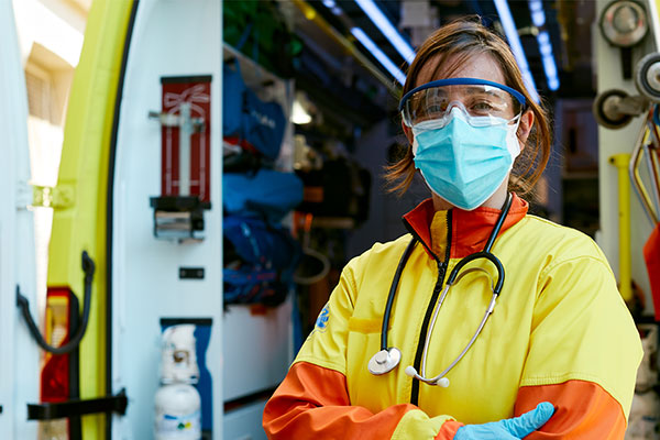 EMS professional wearing personal protective equipment and standing in front of an ambulance