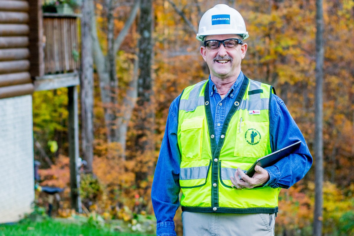 Dan Hughes smiles while wearing safety gear and holding a tablet