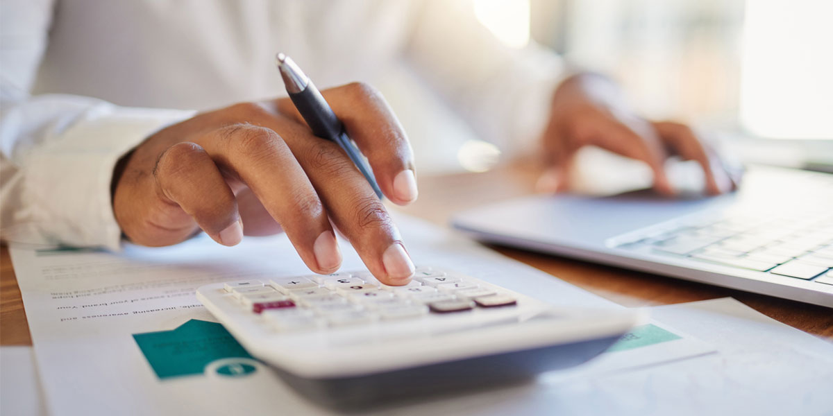 close up photo of hands using a calculator and laptop keyboard on a desk