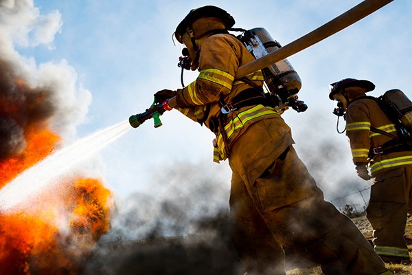 A firefighter sprays a large fire with a fire hose.