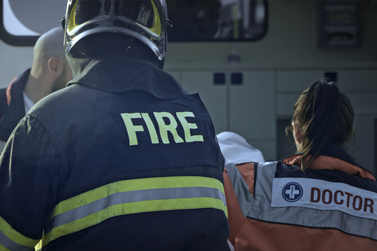 photo of first responders from behind, one dressed as a fighter and one dressed as an emergency medical technician