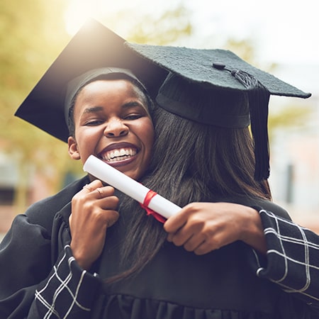 graduate with diploma hugging another graduate