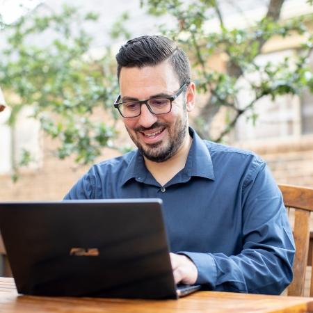 A man is working on a laptop while sitting outside