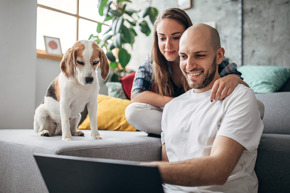 student with their partner and dog sitting on a couch and looking at a laptop computer