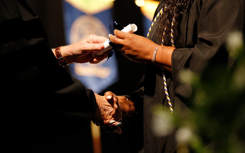 Graduate shaking hands with someone while being handed a diploma.