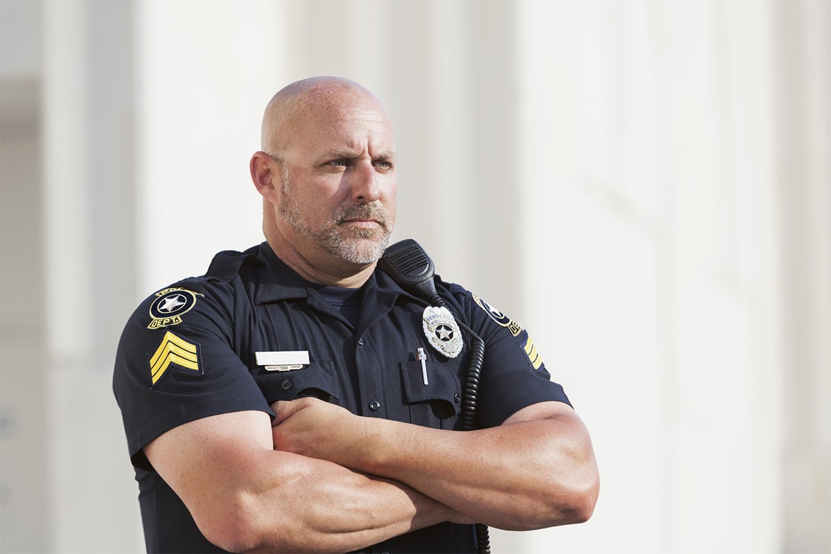 A police officer crosses his arms and looks off in the distance with furrowed brows.