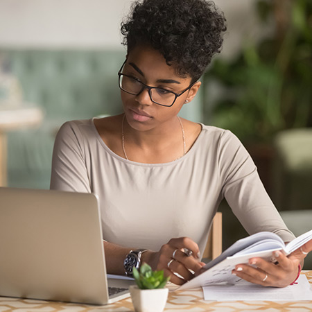 Student flipping through book while referencing laptop