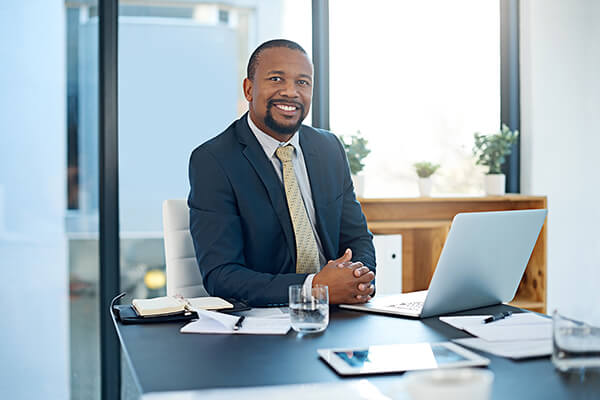 Man in business suits smiles from his desk
