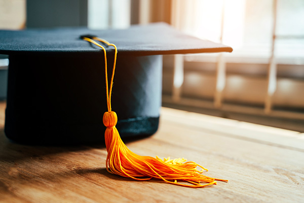 black graduation cap with a gold tassel on top of a wood table