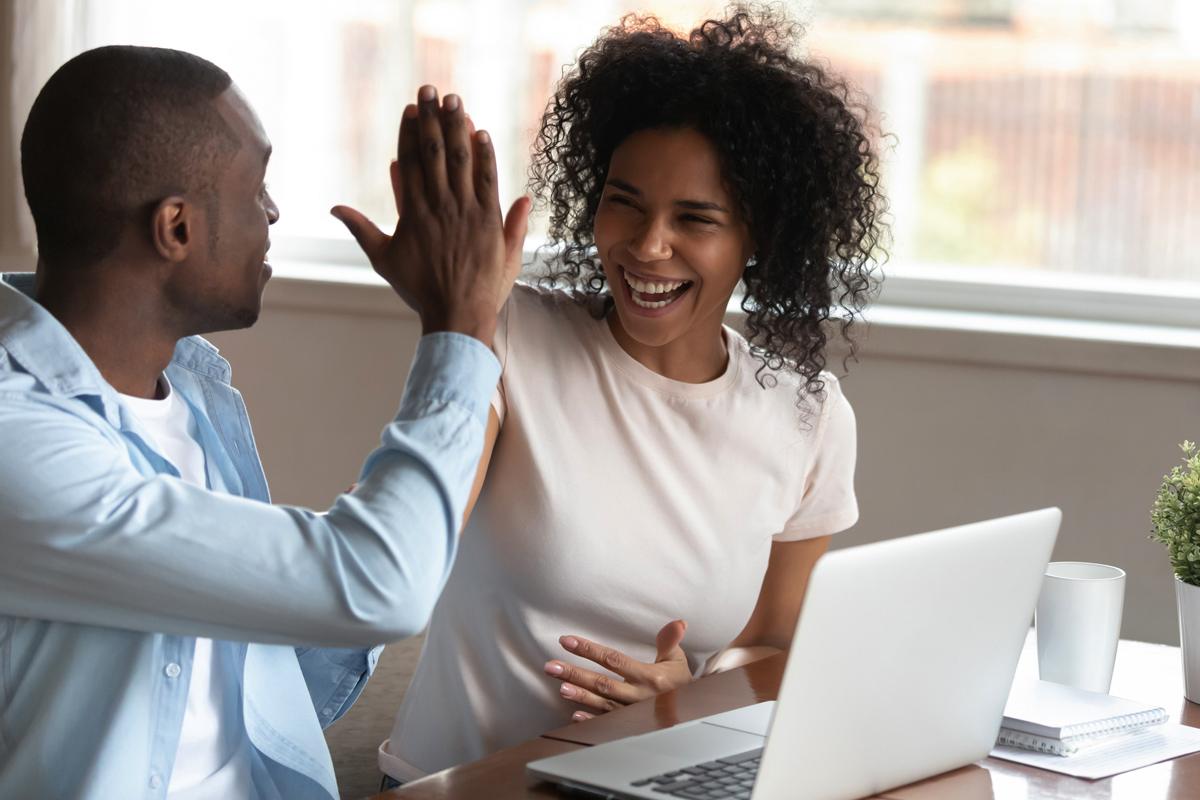 A couple high fives at a desk with a laptop.