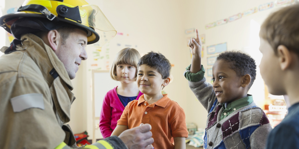 firefighter smiling and speaking with children in a classroom