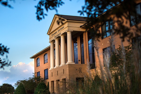 View of the CSU building facade peeking through tree leaves and dune grass.