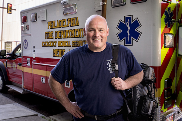 EMS professional holding a bag and standing in front of an ambulance from the Philadelphia Fire Department