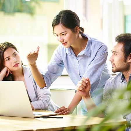 Three coworkers problem solving at desk with laptop