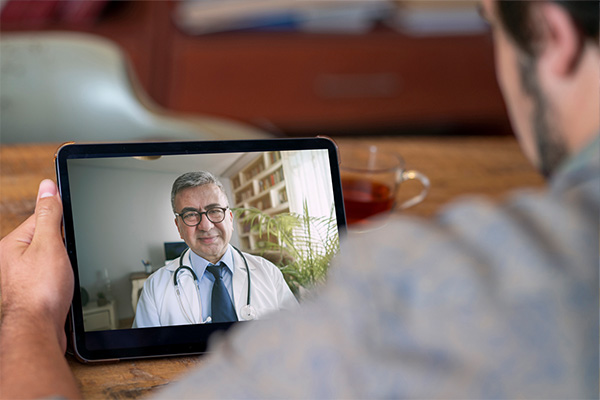 Person sitting at a table and talking to a doctor using video chat on a tablet