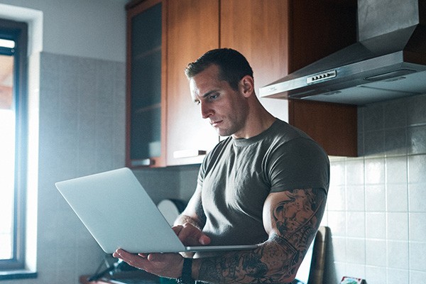 An off duty military man works on a laptop in his kitchen.