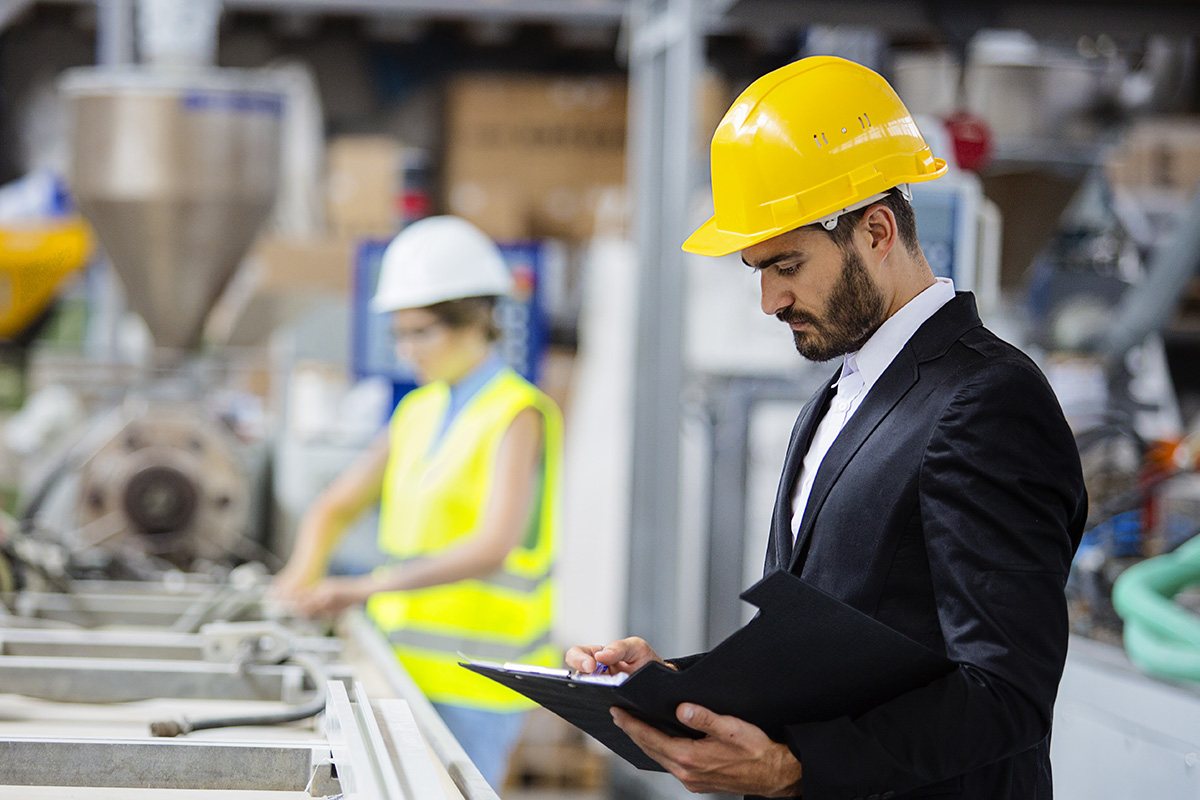 A man in a business suit and hard hat looks over paperwork as he inspects a work site.