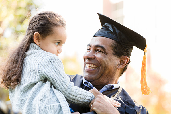 College graduate with a cap and gown smiling and holding a child in their arms