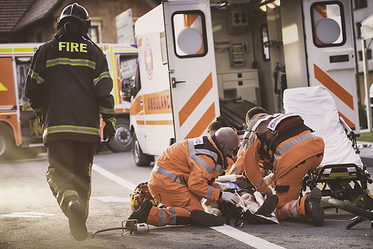 A group of EMTs attend to an accident victim on the road behind an ambulance.