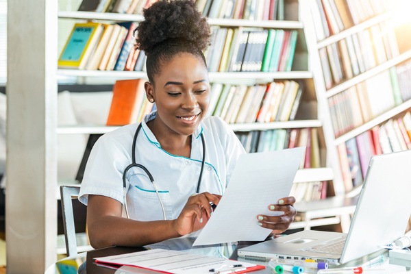 A young woman in scrubs looks over paperwork.