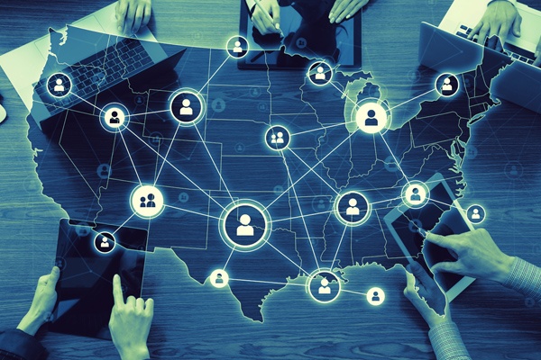 US map with network of user icons overlays a table with several people using laptops and tablets.