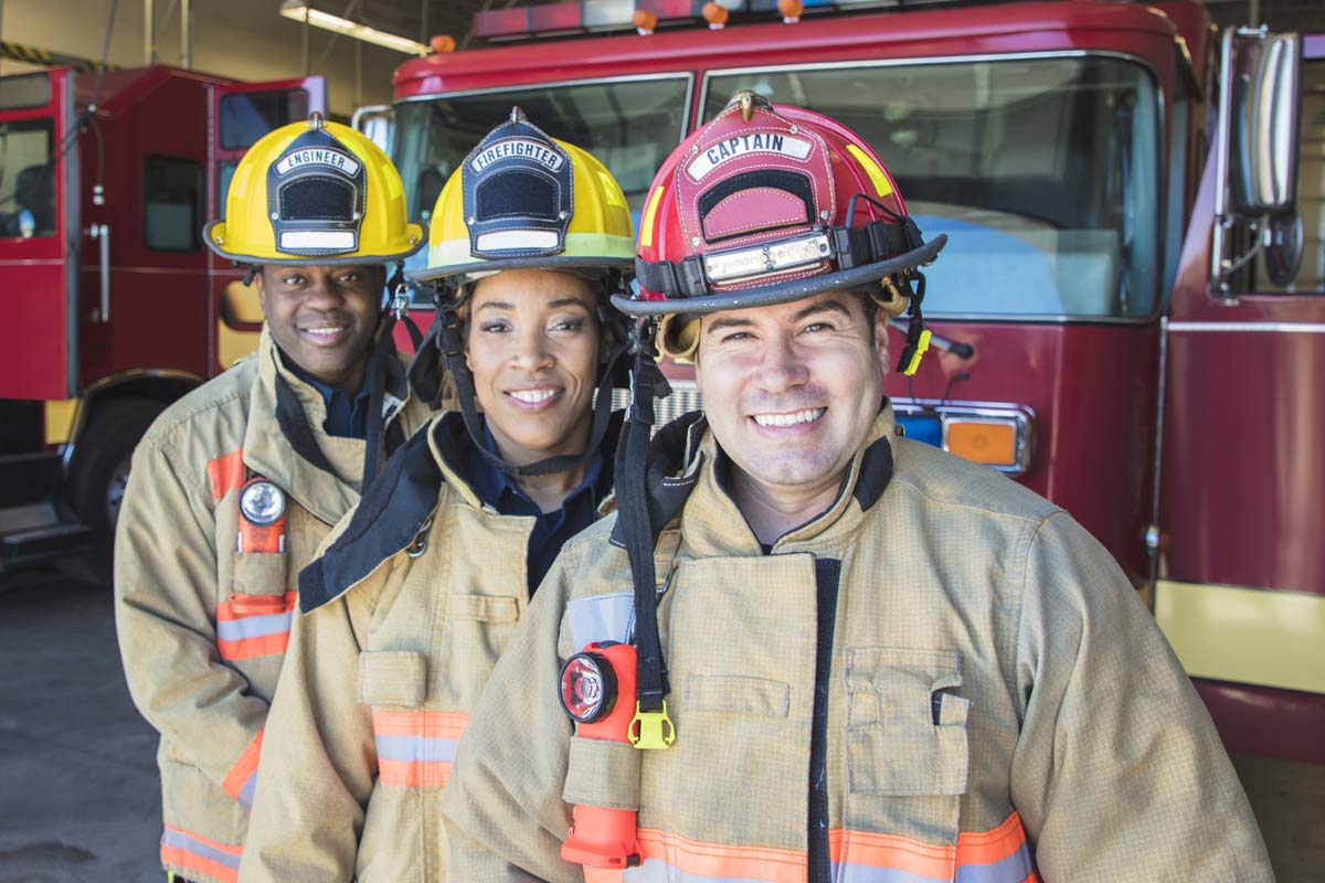 three firefighters posing in front of a fire truck parked inside the fire station