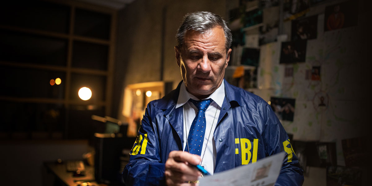 crime scene investigator wearing an FBI jacket standing in an office and looking down at a sheet of paper