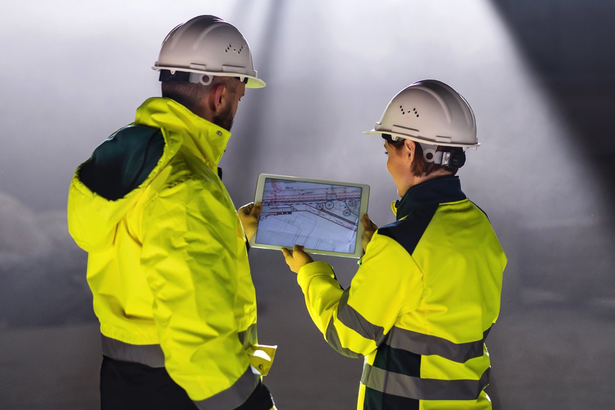 Two safety workers look at plans on a tablet.