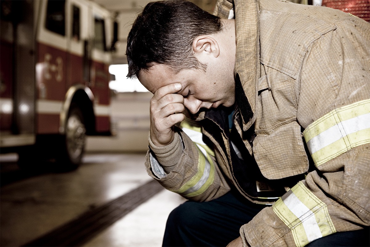 A firefighter sits with his head in his hand.