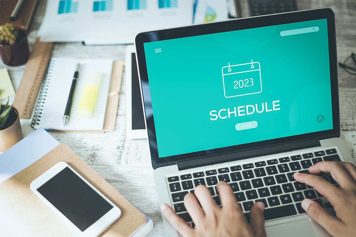 Hands typing on a laptop on a desk, the screen shows a calendar icon and the word "schedule"