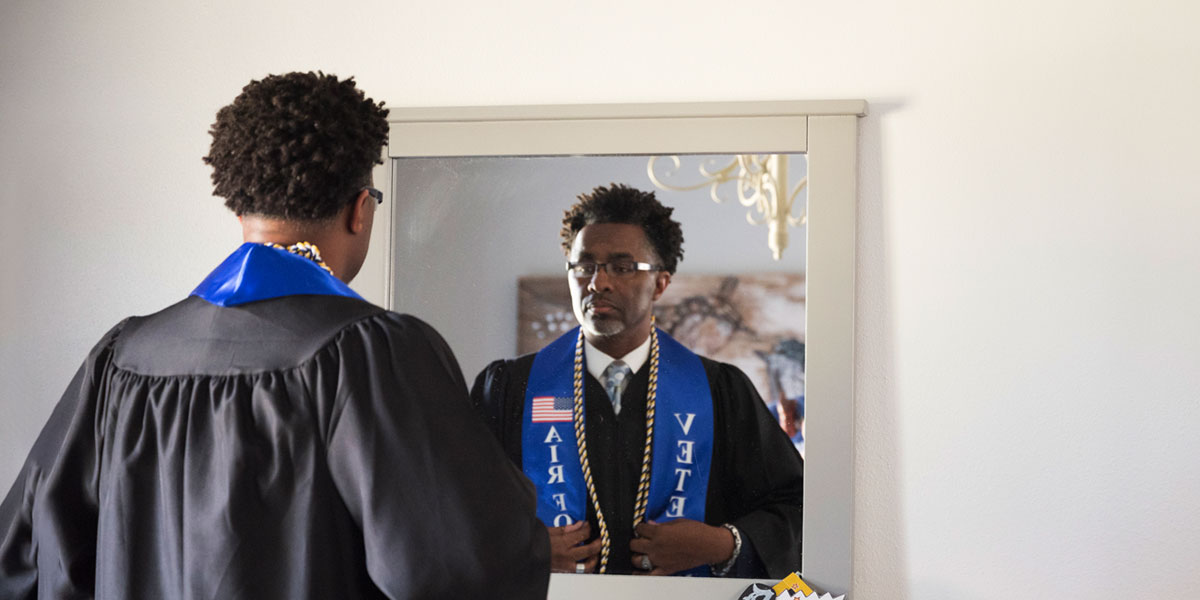 Columbia Southern University graduate and veteran Michael Beard in a graduation gown looking in a mirror