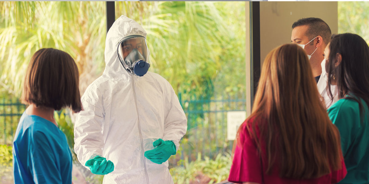 emergency management professionals, including one wearing a hazmat suit, standing in a circle and talking