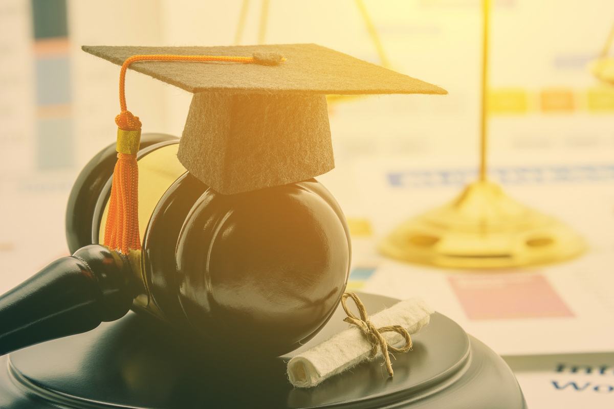 A miniature graduation cap sits atop a gavel resting next to a miniature diploma.