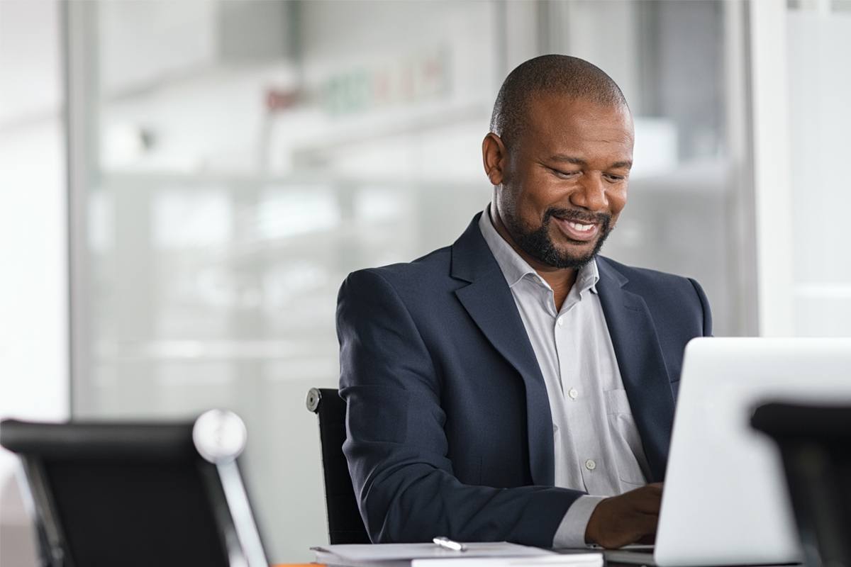 A man in a business suit smiles down at his laptop