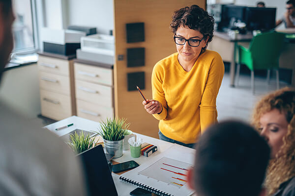 A woman holds a pencil absentmindedly as she reviews charts in a meeting.